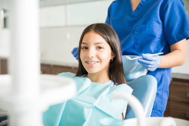 Dentist Standing Behind Smiling Teenage Girl With Braces In Clinic Portrait of smiling teenage girl with braces sitting on chair while dentist standing in clinic orthodontist stock pictures, royalty-free photos & images