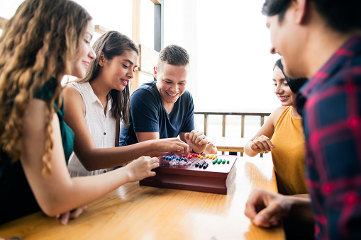 A group of young people sitting face to face at a table, playing a board-game and enjoying themselves.