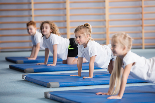 Happy girl exercising on blue mat during corrective gymnastics classes
