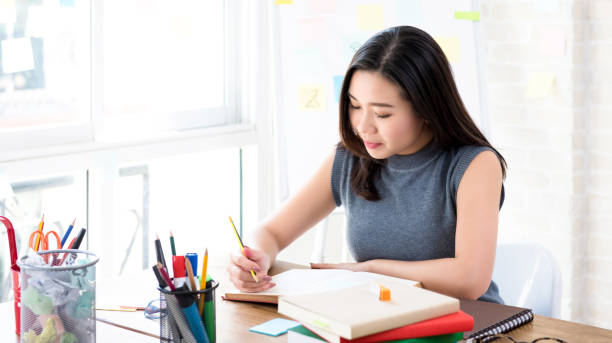 Asian female college student reading book at the table Young Asian female college student concentrating on reading book at the table preparing for examination dissertation stock pictures, royalty-free photos & images