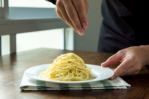 Chef seasoning Italian spaghetti with ground parsley on white dish at kitchen island