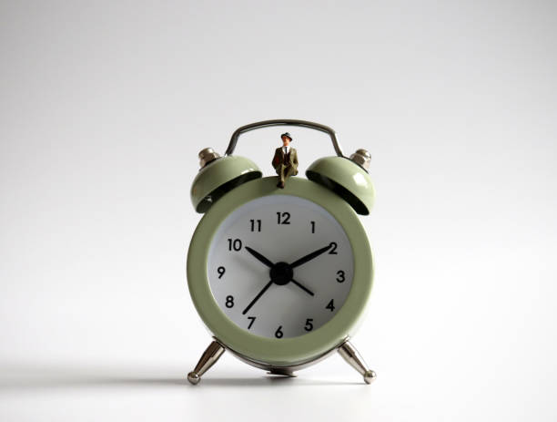 istock A miniature man sitting on the alarm clock. 988116518
