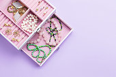 Open jewelry box with neclaces, earrings and rings on pastel background. Top view