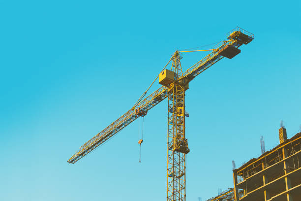 istock Yellow tower crane at construction site on blue sky background toned 988186176