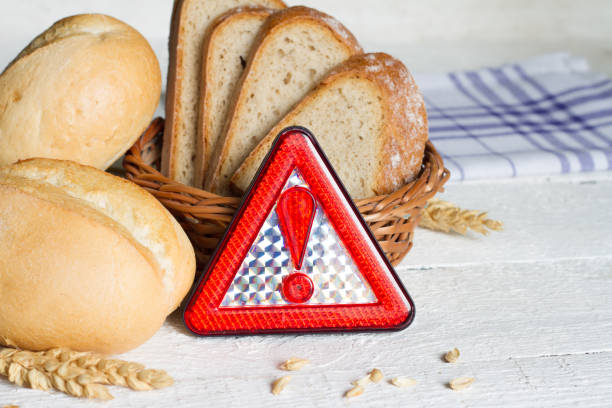 Gluten intolerance with bread wheat and warning sign on white planks