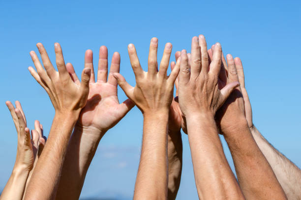istock Group of people pulling hands in the air in sunlight. Many hands against blue sky background 988201700