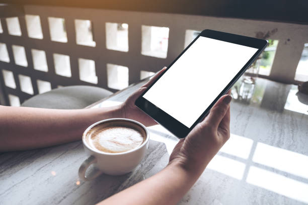 istock Mockup image of a woman holding black tablet pc with white blank screen with coffee cup on table 988211968