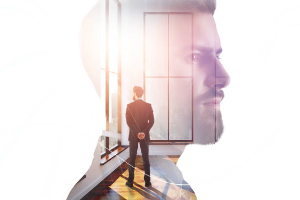 Businessman looking out of window in abstract interior with sunlight and colleague. Lifestyle and employment concept. Double exposure