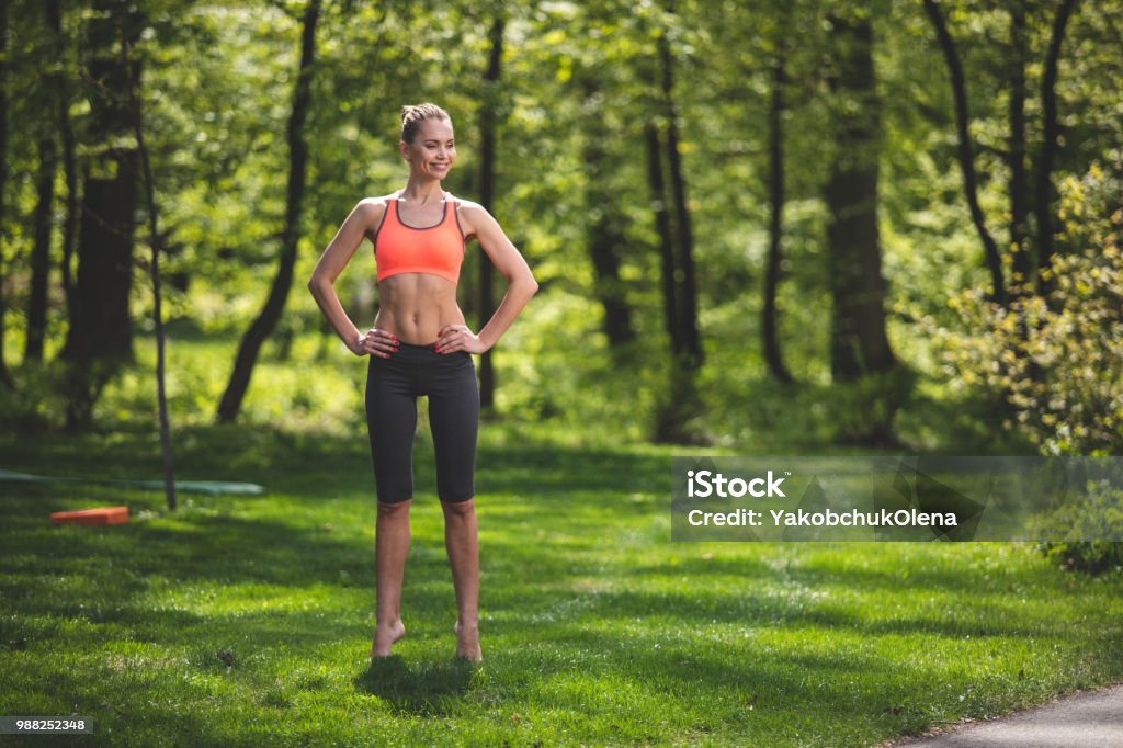 Cheerful lady is tiptoeing on grass Smiling lady is standing on toes and holding hands on waist on green lawn. She is enjoying exercising in beautiful countryside. Copy space in right side Tiptoe Stock Photo