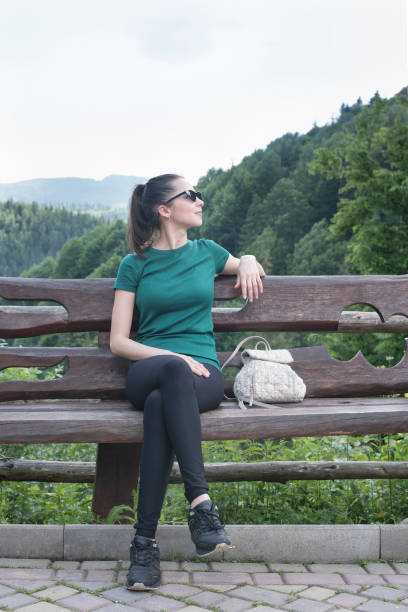 istock Girl with a backpack sitting on the bench. Forest on background 988253728