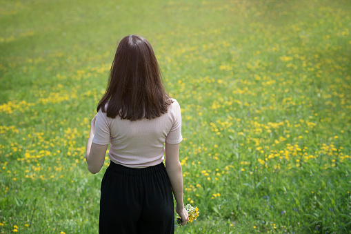 Young woman is standing on a flower meadow. Summer sunny day. Back view