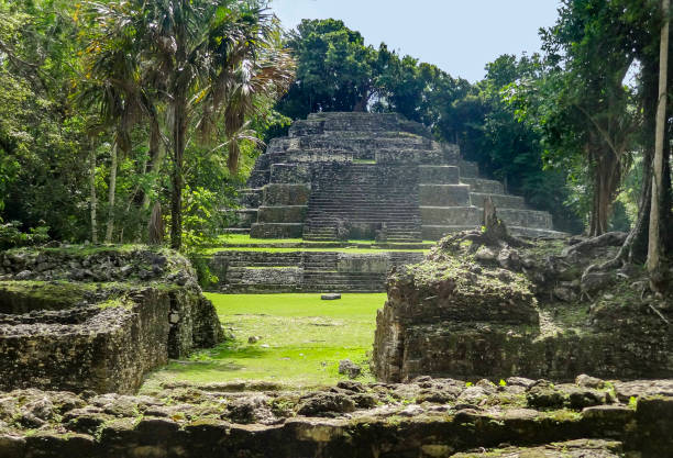 Wide shot of tourists dwarfed by the Temple of the Jaguar Mayan pyramid in Lamanai, Belize