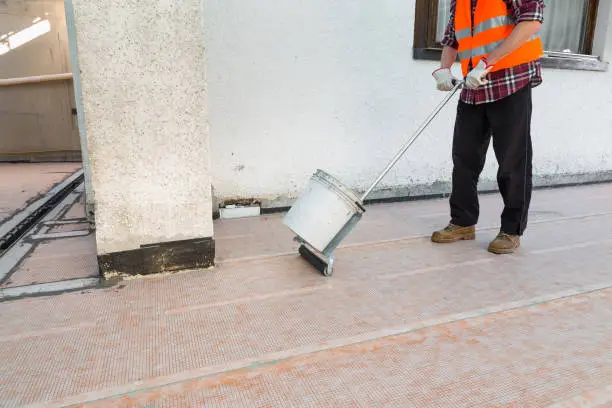 Worker whith a roller, on a terrace - roof, is laying a membrane ideal for waterproofing in conjunction with tiled surfaces (ceramic and stone tile) on walls and floors. Tiles can be installed directly above