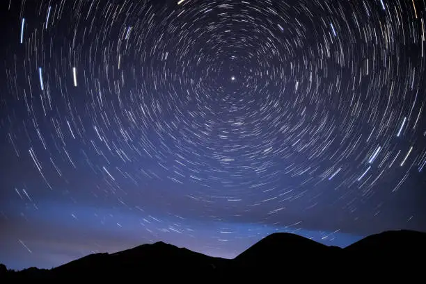 Bright traces of stars revolving around the polar star, in the form of circular tracks and glow in the night sky against the background of the mountains