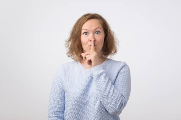 istock Mature woman in blue sweater making silence gesture with forefinger 988322606