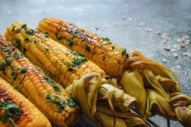 istock Native American cuisine, roasted corncobs with green herbs and sauce on blue marble background, close-up. Grilled corn, healthy eating concept. Selective Focus 988336872