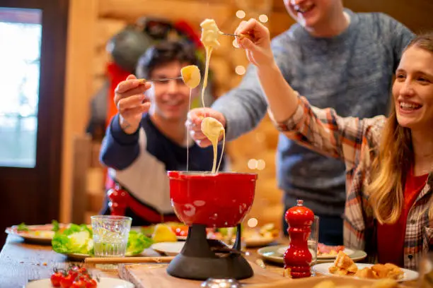 A group of friends eat fondue together at dinner whilst on a skiing holiday.