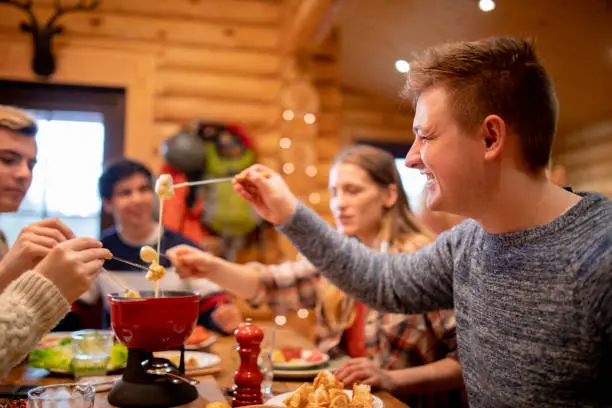A group of friends eat fondue together at dinner whilst on a skiing holiday.