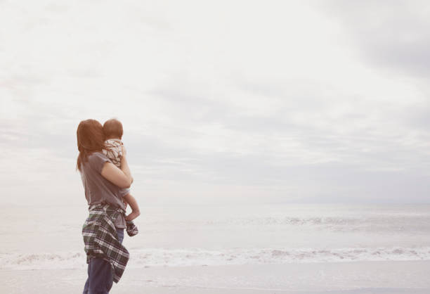 An asian mother carrying her baby boy on the beach.