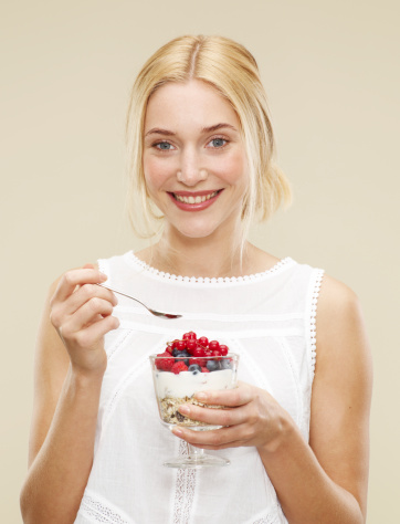 female, blonde hair, blue eyes, smile, white vest top, fruit and nut cereal, cereal, blackberries, cherries, blueberries, raspberries, yoghurt, biscuit background, yellow background