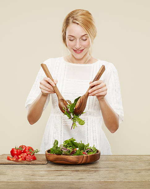 female smiling as she tosses a fresh salad - mixing table fotografías e imágenes de stock