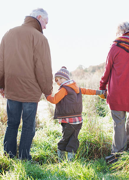 grands-parents tenant mains avec petit-fils - generation gap multi generation family vertical holding hands photos et images de collection