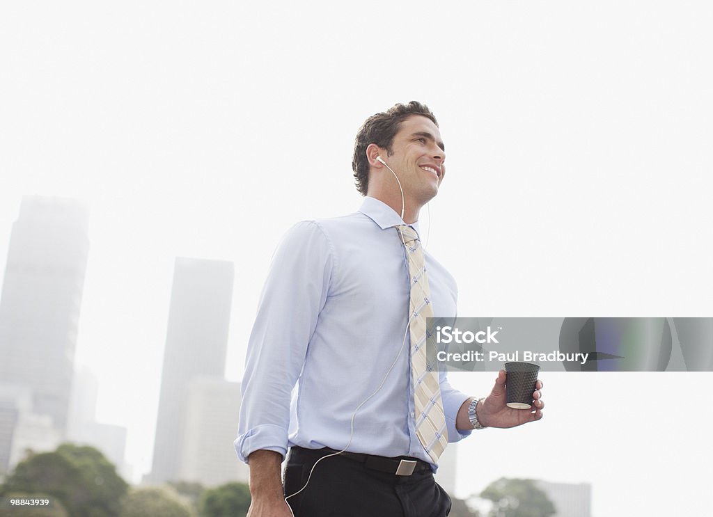 Businessman listening to headphones and carrying coffee  Australia Stock Photo