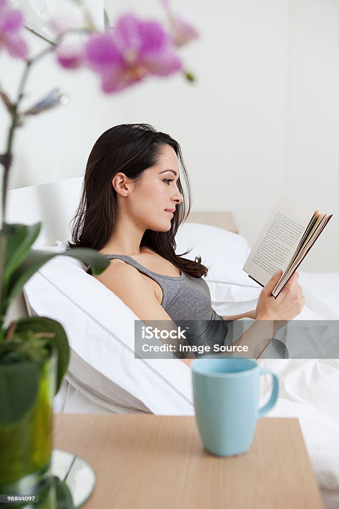 Giovane donna leggere a letto - Foto stock royalty-free di Adulto