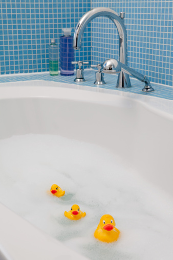 Toy yellow duck in a miniature white bathtub covered with soap bubbles. Bath time concept.