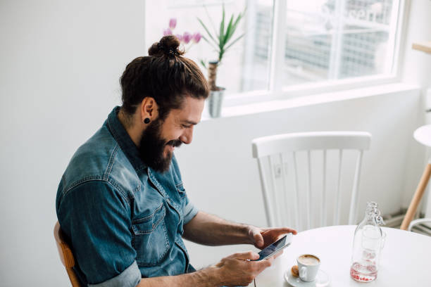 istock Smiling young man typing on his phone at a coffee shop 988466528