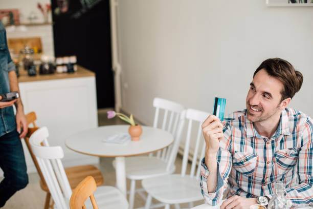 istock Happy man holding credit card while sitting at coffee shop 988468246