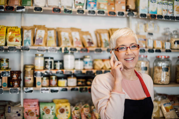 istock Smiling mature woman using mobile phone at the store 988478578