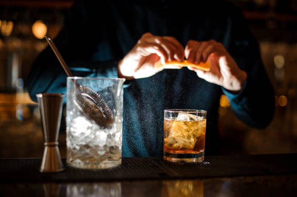 barman finishes preparing an alcoholic cocktail old fashioned adding an orange bitter - drink on top of ice food imagens e fotografias de stock