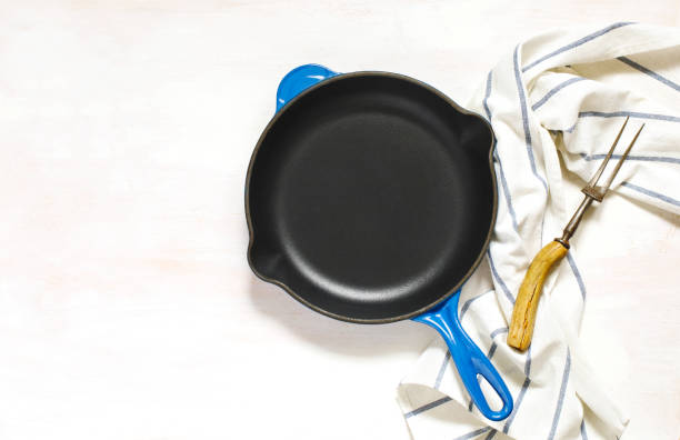 istock Blue empty cast iron frying pan and meat fork on white background, top view 988486368