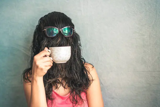 Woman's face is covered with hair while she drinks coffee in the cup