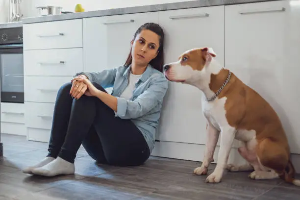 Photo of Sad woman sitting on a kitchen floor with her dog