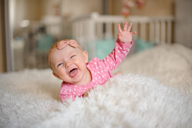 Little laughing girl with a bow on her head lying on the bed stock photo