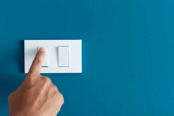 A finger turning on lighting switch on rough on blue dark wall. A finger turning on lighting switch on rough on blue dark wall. Empty space for text your switching stock pictures, royalty-free photos & images