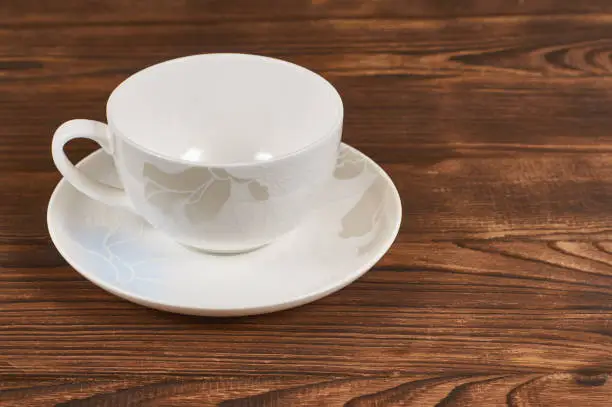 clean white cup and saucer with delicate ornament on wooden background