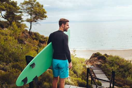 A man is holding his surfboard near the sea on the beach. He's ready to go surf.