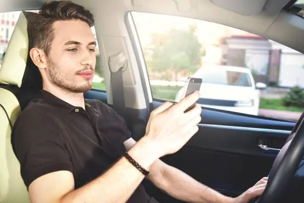 Photo of Photo of a handsome man using mobile phone while driving.