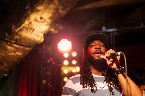 An African American male singer with dreadlocks is singing at stage during a live music event.