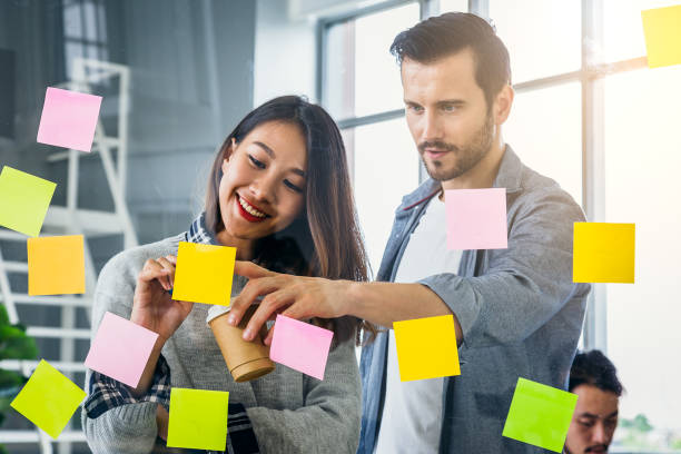 istock Young creative business people using notes papers and discussing for new project behind glass wall at modern office 988540858
