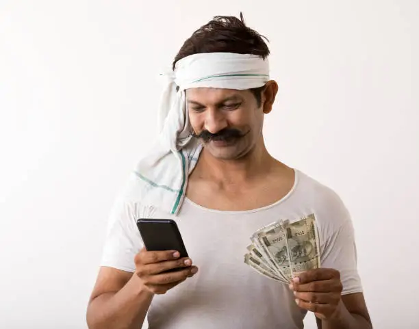 Indian farmer holding paper currency and using mobile phone