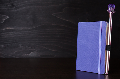 Purple notepad with an attached pen on the table on a black woodenl background