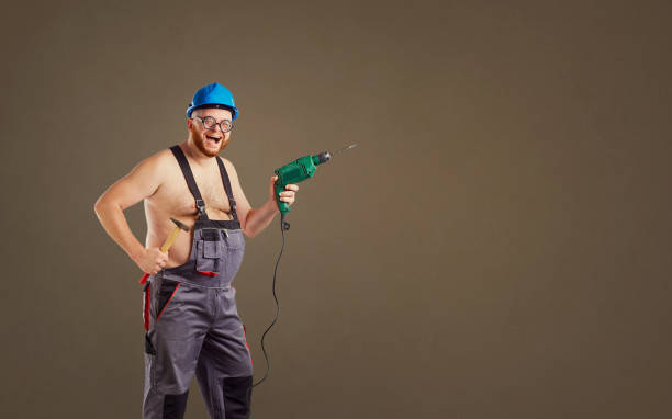 istock The overweight funny man builder with a drill 988573590
