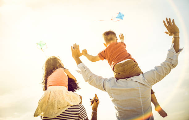 happy multiracial families group with parents and children playing with kite at beach vacation - summer joy concept with mixed race people having fun together at sunset  - warm bright sunshine filter - spring happiness women latin american and hispanic ethnicity imagens e fotografias de stock