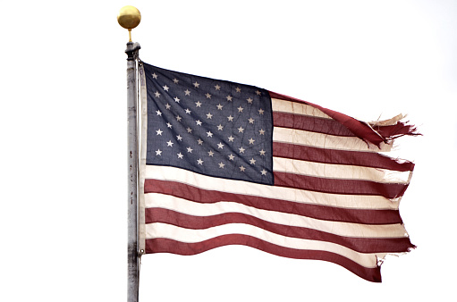 Flag of the United States of America with stars and stripes waving hanging from the pole to the right, ruined and frayed, in a plumb sky