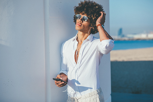 Young handsome man standing at the beach and using phone