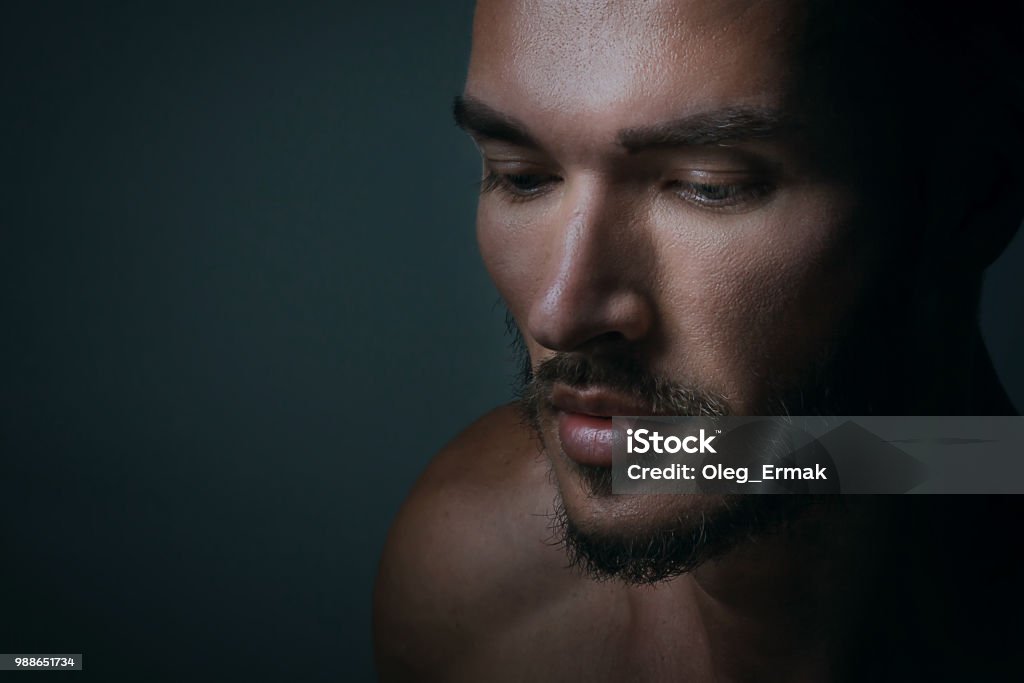 Close up portrait of a handsome young man with brave manly face on dark background. Caucasian man staring serious, male beauty, cosmetics. Men Stock Photo